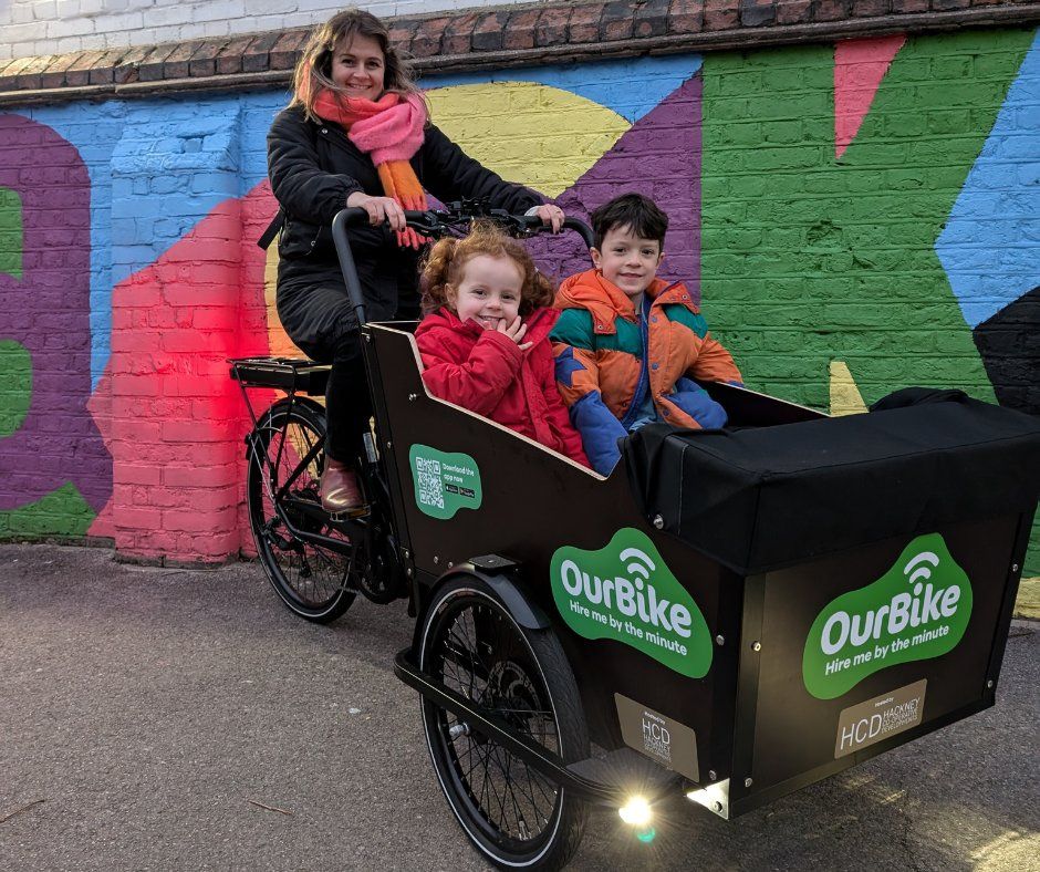 a woman riding a cargo bike with two children in the front carrier
