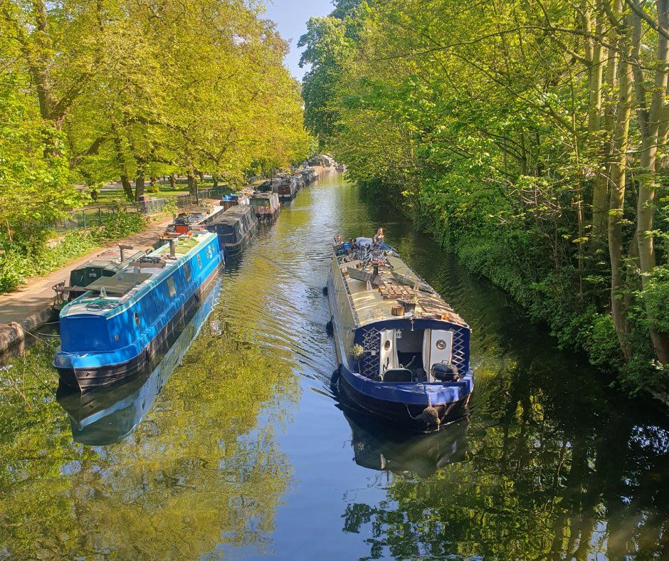 A canal boat travels down a canal in London next to moored boats