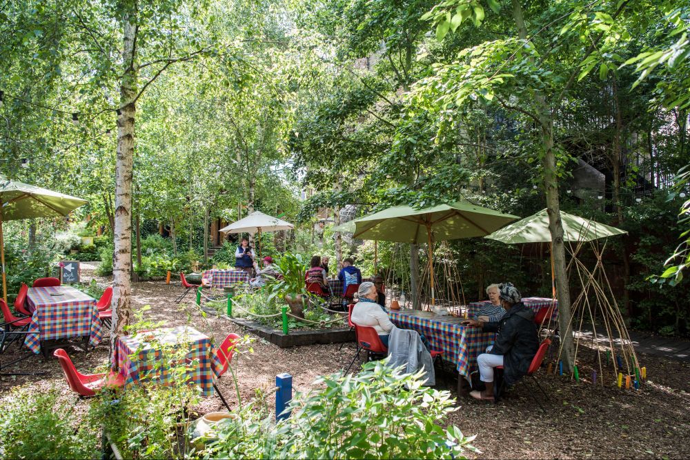 a group of people sitting at tables in an outdoor garden