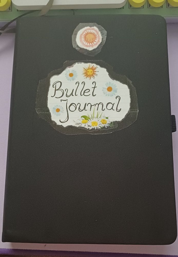 schwarzes notizbuch a5 auf dem vorn "bullet journal" drauf steht, dekoriert mit diversen stickern