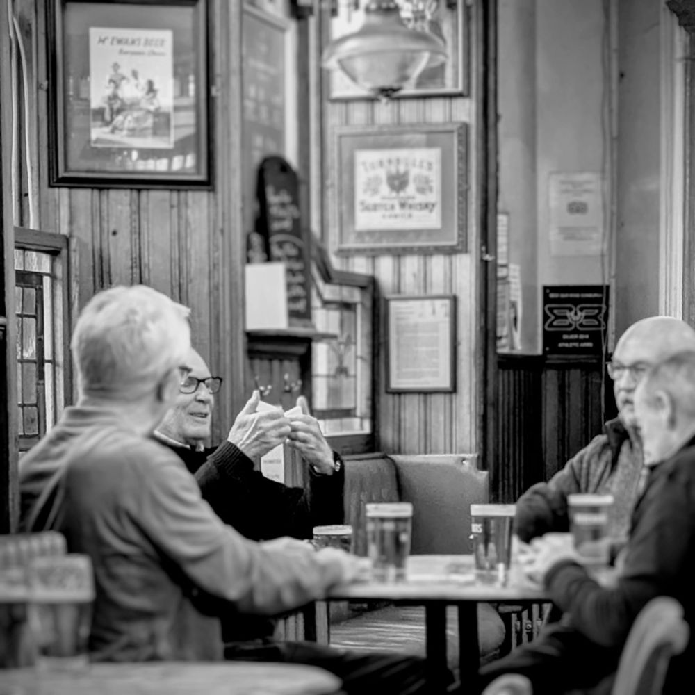 A black and white photograph showing four friends playing dominoes in a pub