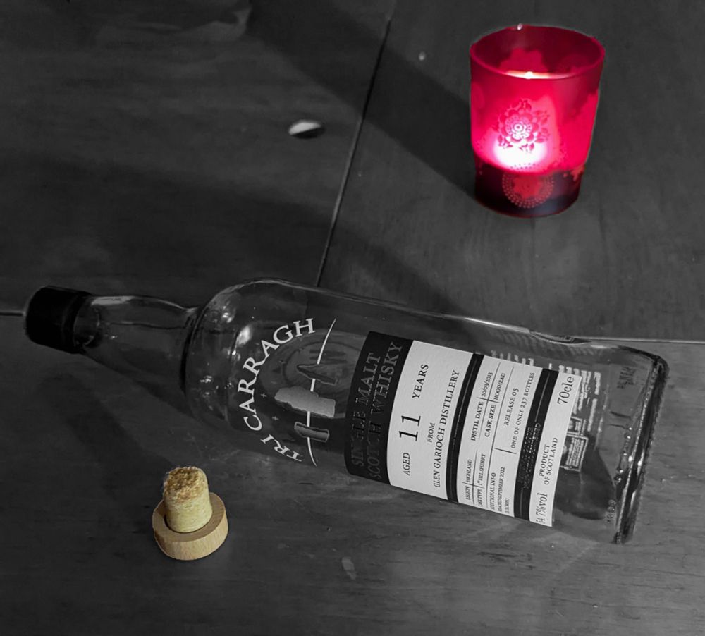 A photograph of an empty whisky bottle lying on its side in Black and White with a red candle cork. 