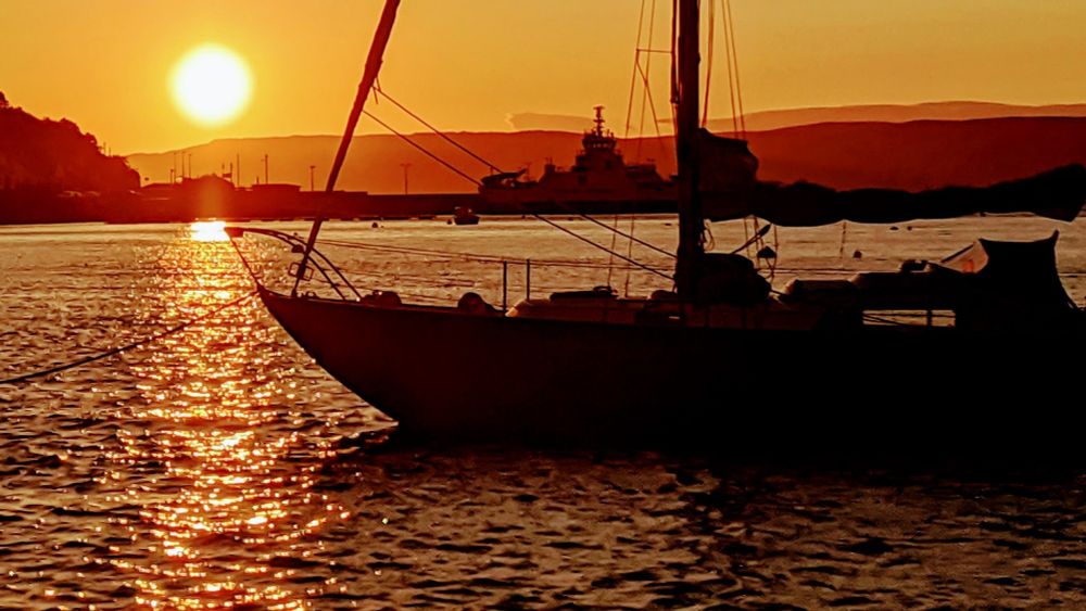 Sunset with a sailing boat in shadow in the foreground.