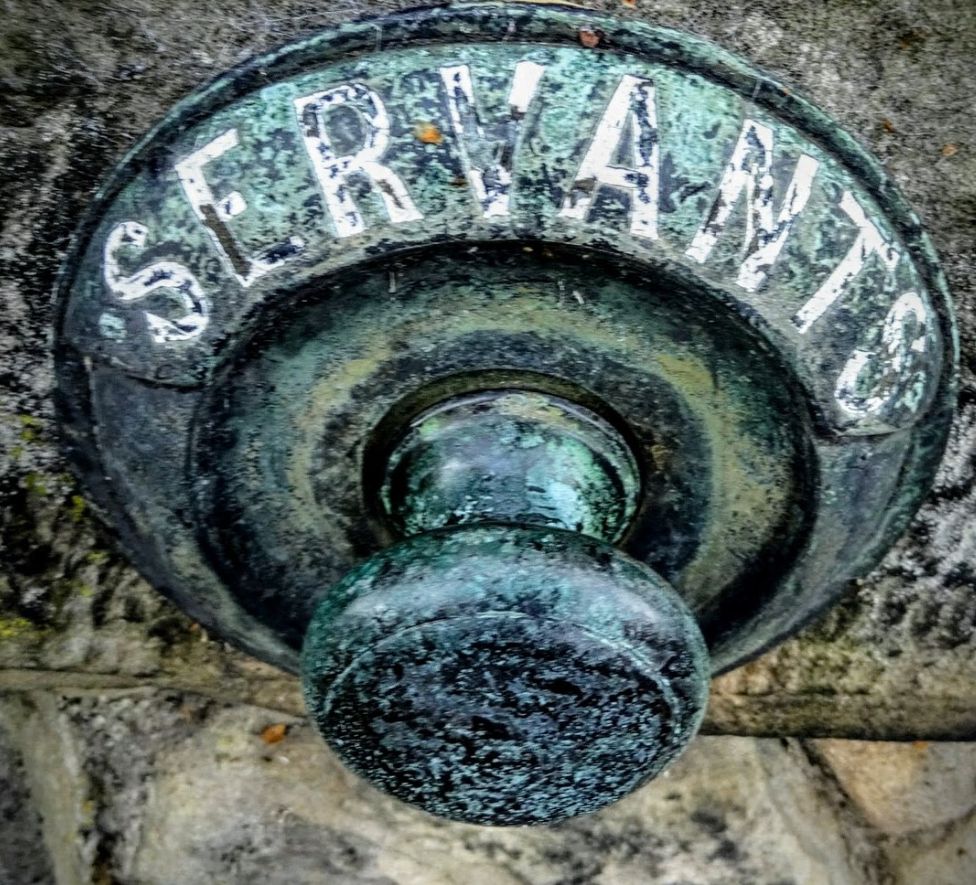 A rusty old bell pull set into a wall with "servants" written above the pull.