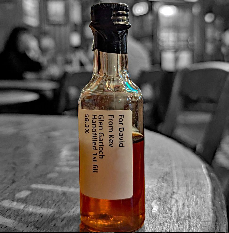 A small bottle of whisky on a table in a pub. The background colour has been removed and it is in Black and white.