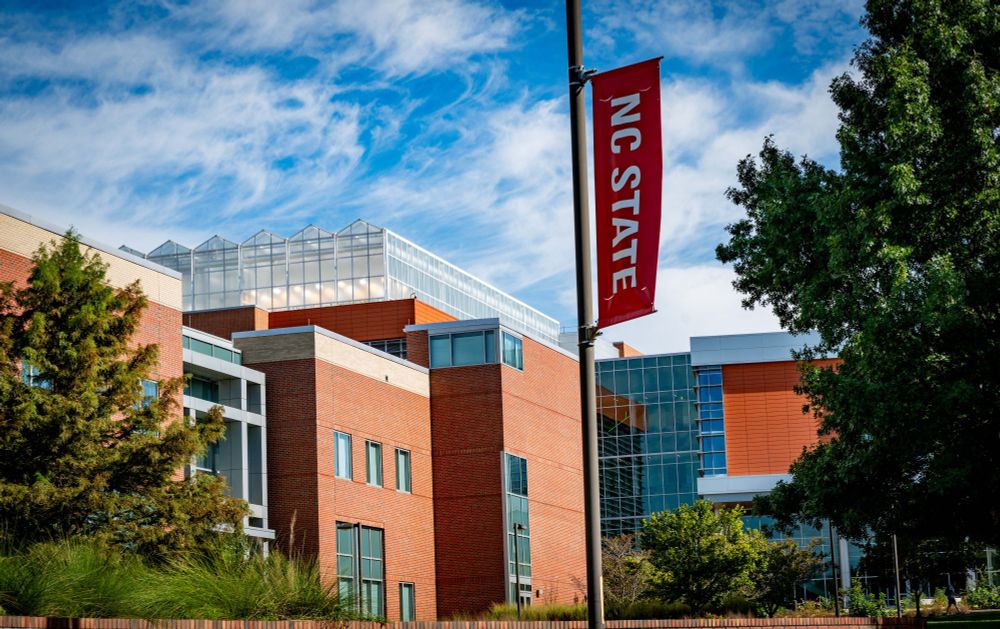 NC State main campus, brick building with NCSU flag hanging on a sunny day.