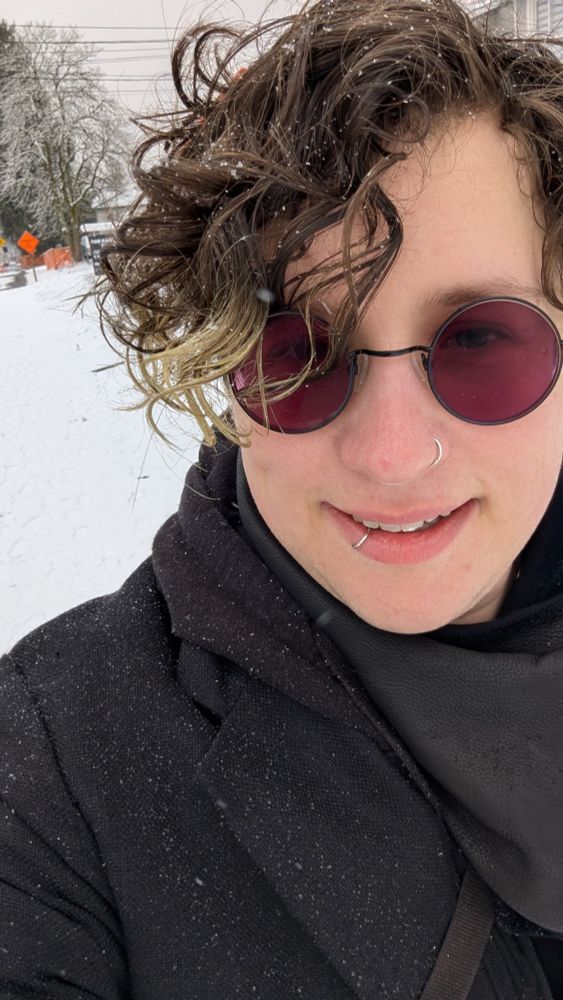 Selfie of a smiling person with curls and round sunglasses bundled up warm and going for a walk in the snow
