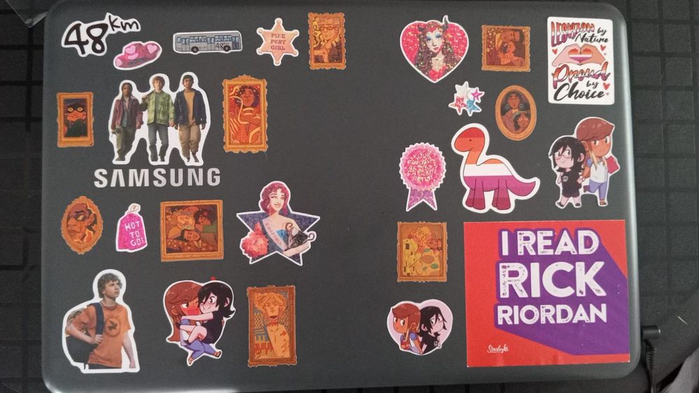 Foto um notebook cheio de adesivos de: Entrevista com o vampiro, Percy Jackson, 48km e Chappell Roman 