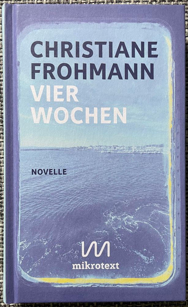 Buchdeckel: Text „Christiane Frohmann, Vier Wochen, Novelle, mikrotext“, im Vordergrund ist blaues Meer, im Hintergrund eine Küstenstadt erkennbar