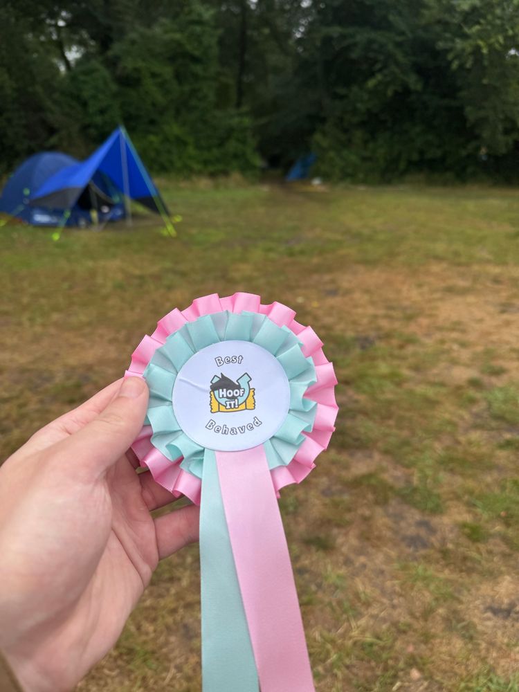 Chip holding up his “best behaved” rosette with a background of woods and a tent. 