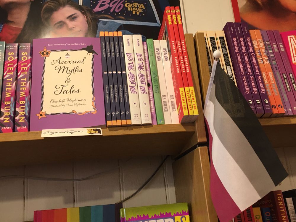 Asexual Myths & Tales on a bookshelf next to an ace flag