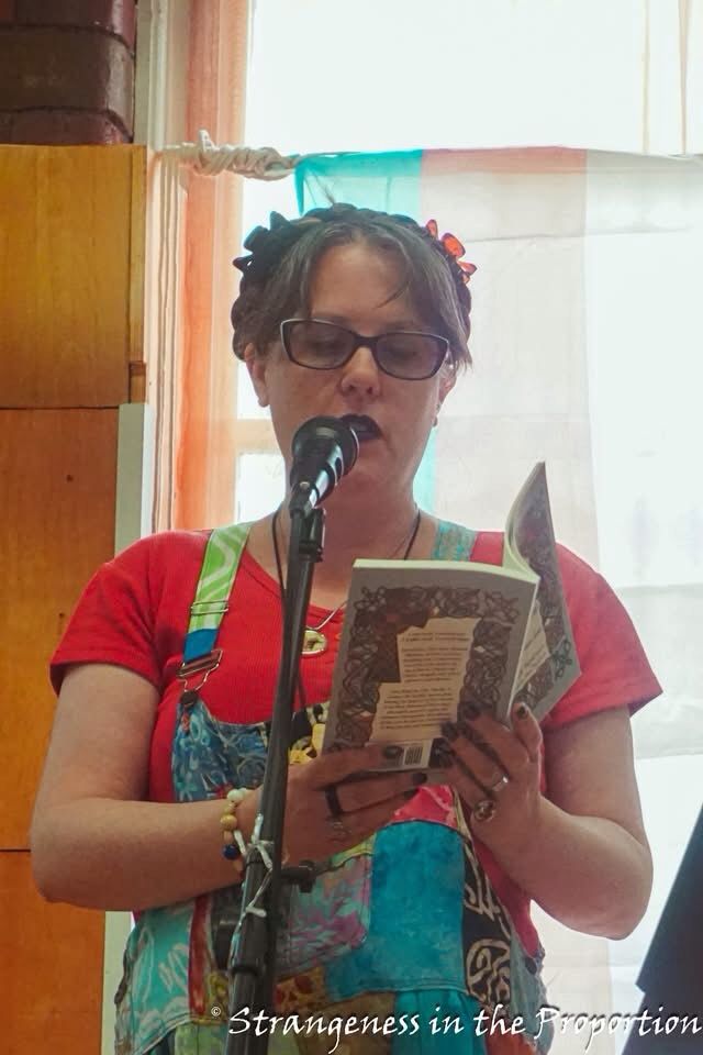 Elizabeth (white, female presenting with dark hair & patchwork dungarees) reading aloud.