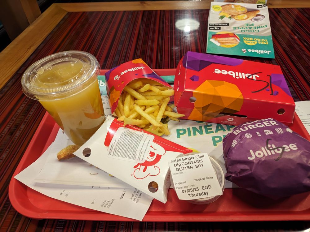 A tray of food from Jollibee, a Filipino restaurant chain. There is a wrapped burger, an open container of fries and additional items, such as a dip and an unopened pineapple drink.