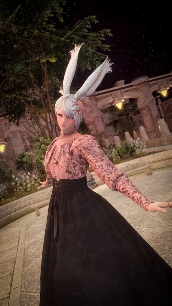 A gpose of Lys, a feminine viera with short, asymetrical white hair, mid-twirl in a light pink, long-sleeved frilly blouse and long, full black skirt with corset-style ribbon ties around the waist and an embossed floral pattern embroidered on both the skirt and blouse. Wearing pink flowers in their hair, they are smiling brightly, looking directly into the camera with a warm expression, and are in the middle of an empty courtyard, backed by shrubs, flowers, and tall trees with the stars shining brightly in the sky behind them. 