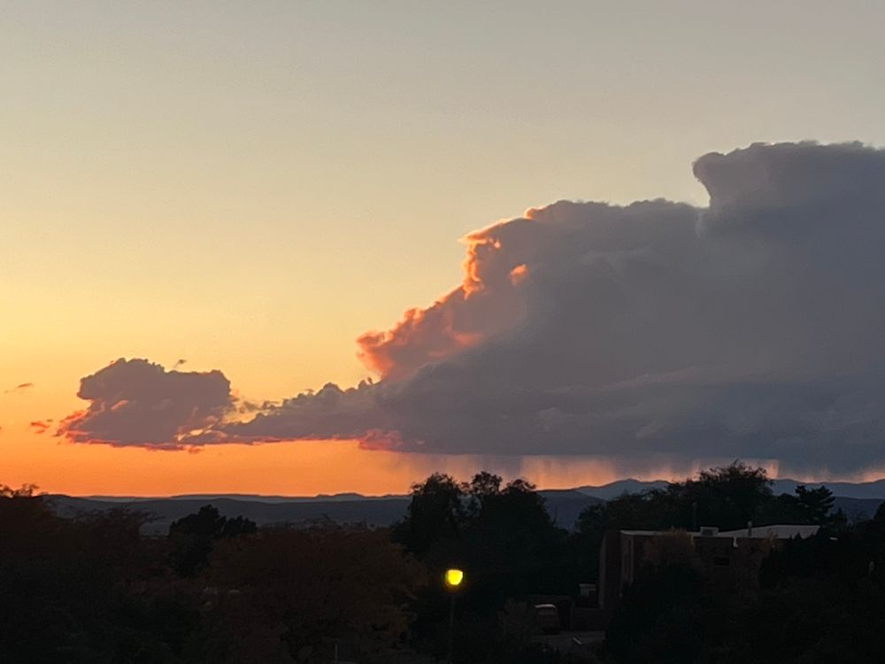 A majestic thunderstorm in the distance, at sunset. The silhouette of the rain shaft is visible.