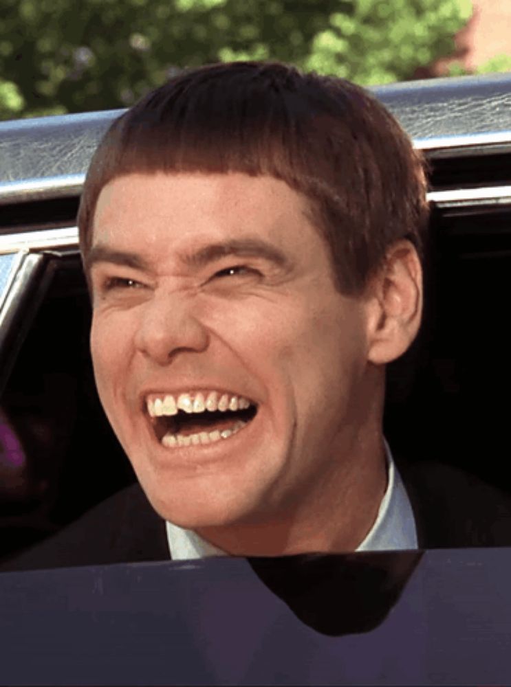 a man with a very short haircut is laughing while sitting in a car