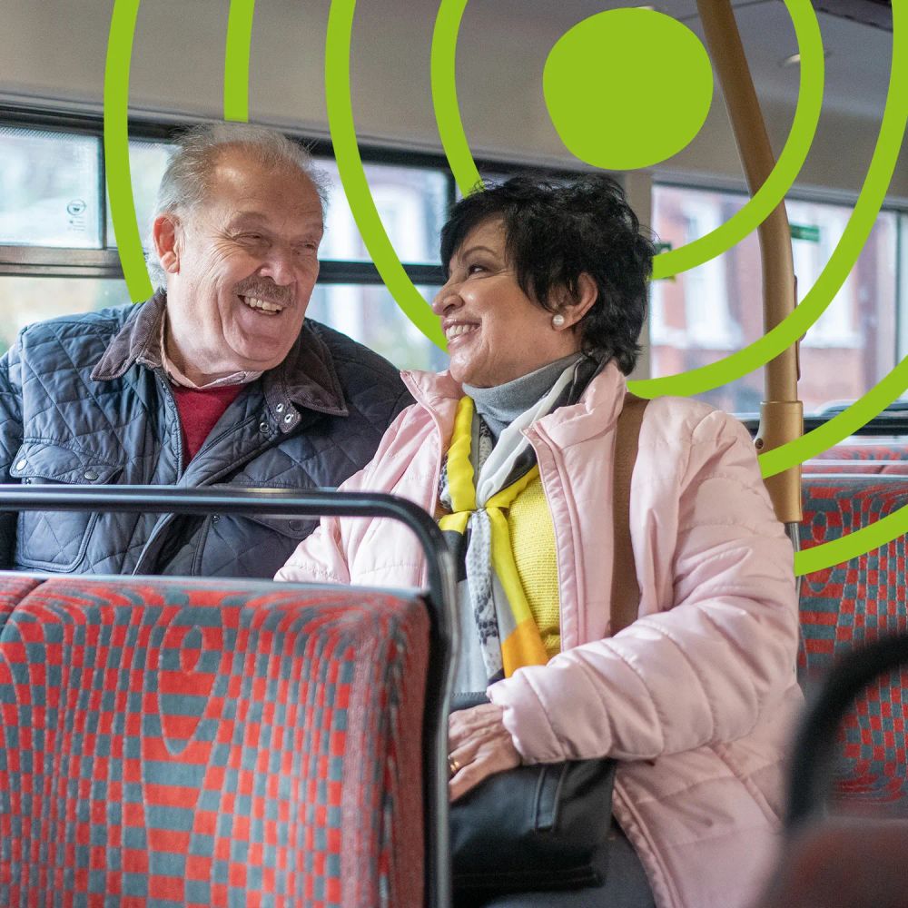 An older woman and older man, riding the bus together while smiling at each other. The UN Decade of Healthy Ageing logo is in the background.