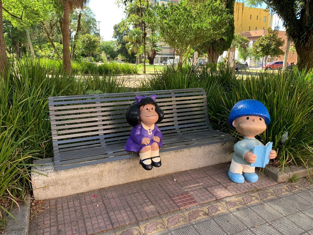 Foto de uma estatua da personagem Mafalda sentada em um banco da Praça Cel. Pedro Osório, em Pelotas. Mafalda está acompanhada da estátua de um menino de cabelo azul (o Betinho), personagem criado pelo cartunista pelotense André Macedo.