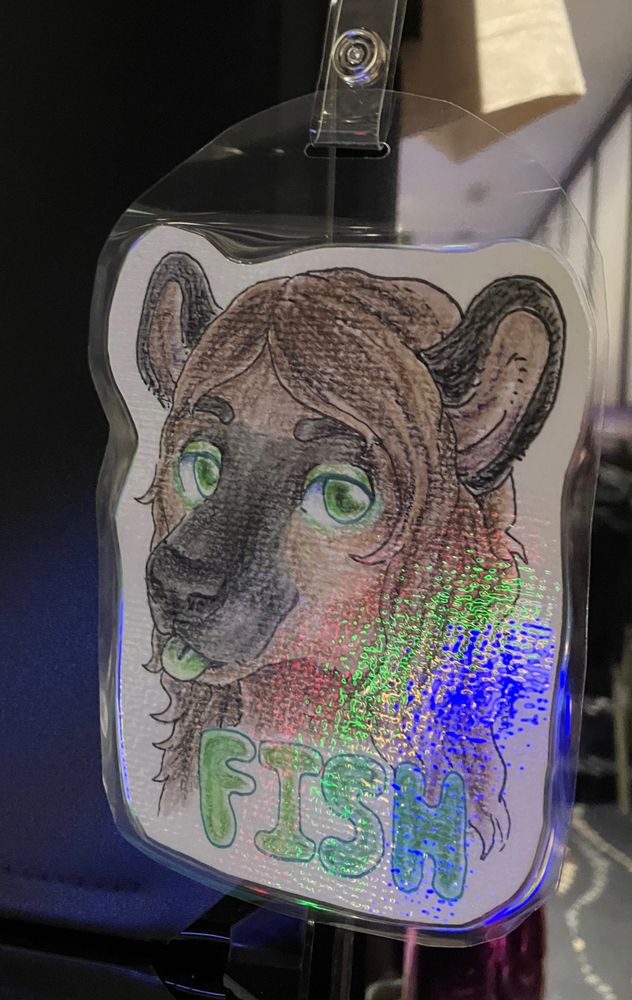 A laminated furry badge of a hyena furry named Fish done in ink, watercolours, and pencil crayon. Character belongs to s.f.starr on instagram