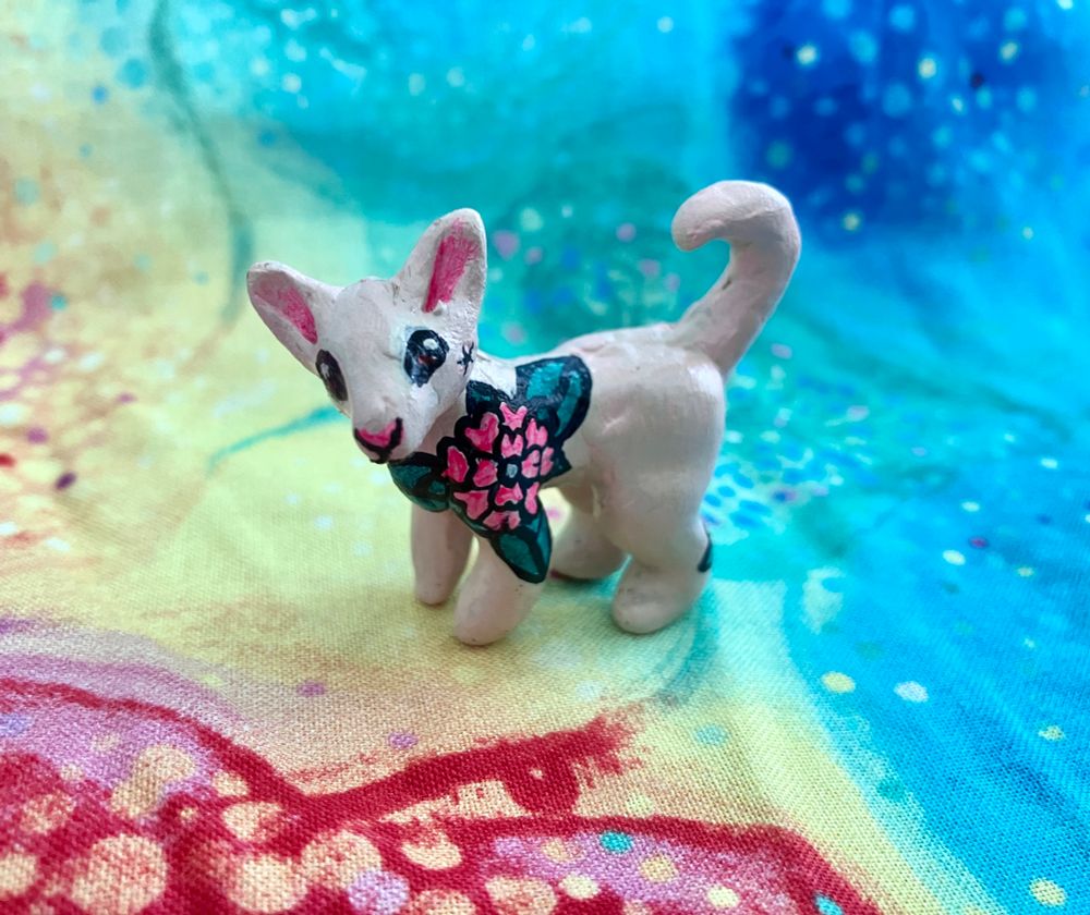A mini polymer clay sculpture of a sphynx cat with uv reactive floral tattoos painted on with acrylic paint