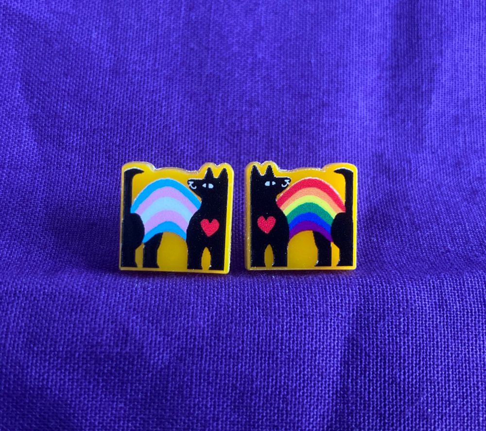 A collection of mini acrylic pins featuring an abstract canine with a rainbow flag or trans flag arch