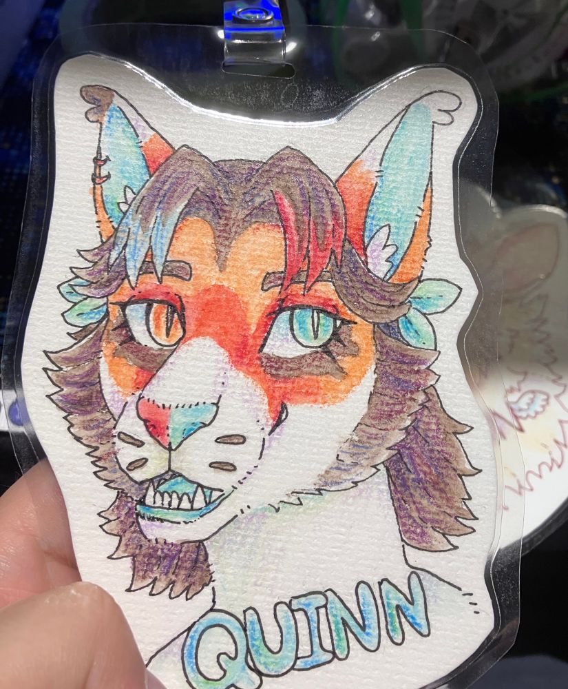 A laminated furry badge of a feline furry named Quinn done in ink, watercolours, and pencil crayon. Character belongs to kim_cat on toyhou.se