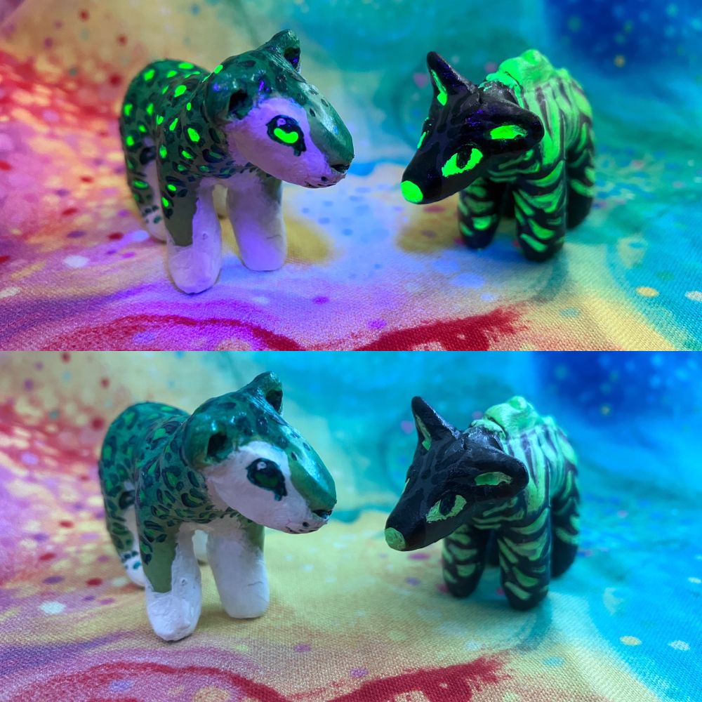 A photo of two sculptures, both mainly green, one is a striped hyena (yeen)and the other is a snow leopard (snep). Two views of them as shown, once under black light and the other under natural light