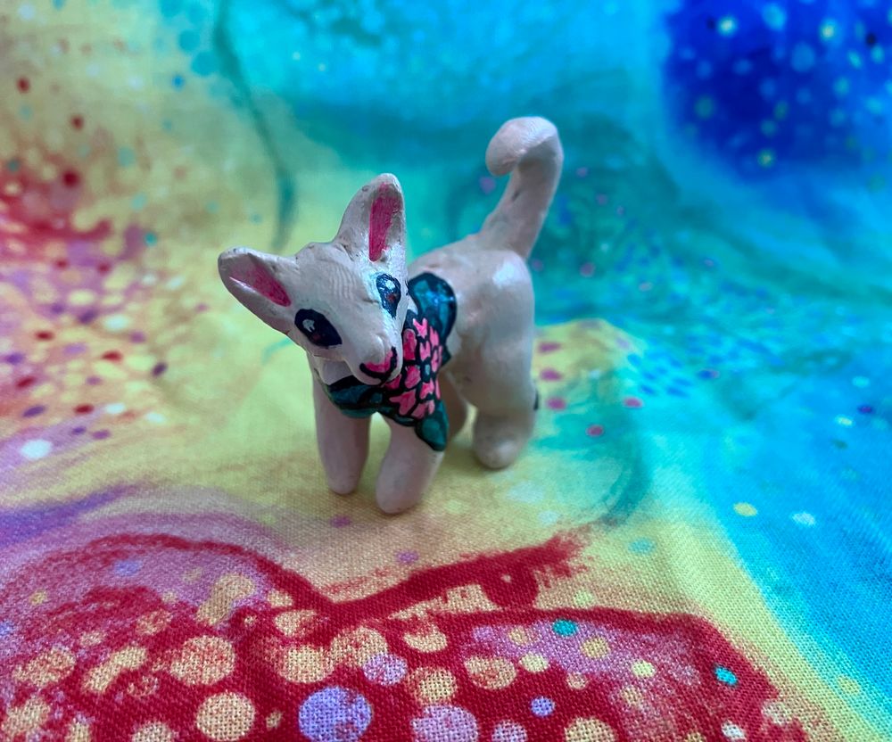 A mini polymer clay sculpture of a sphynx cat with uv reactive floral tattoos painted on with acrylic paint