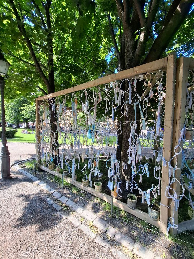 Shreds of multicolured cloth framed in wood... that dances in the breeze. The spaces in between still display some of the surrounding garden park. 