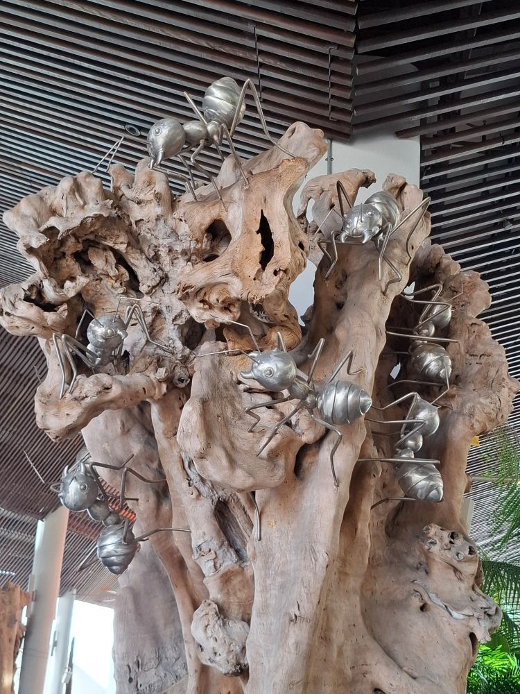 Ant artwork, Gardens by the Bay, Singapore. Large silver metallic ants adorn a gnarled brown red  tree trunk
