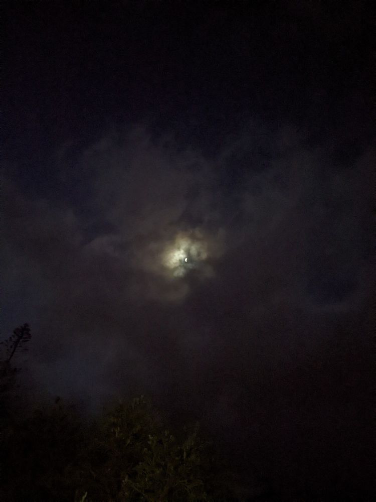 A bright moon barly illuminating a small spot of cloud in a dark and cloudy night