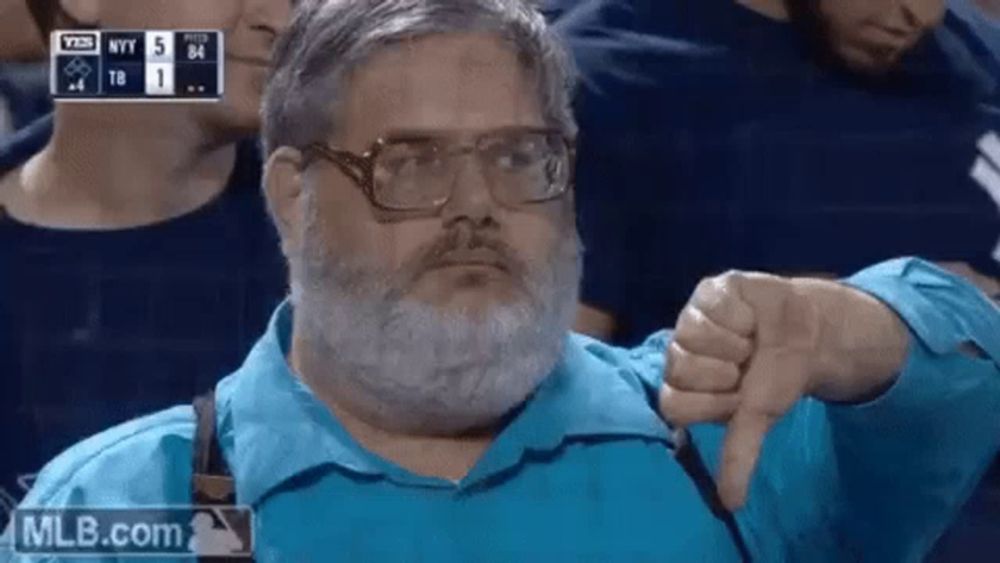 a man with glasses and a beard is giving a thumbs down sign while watching a baseball game .