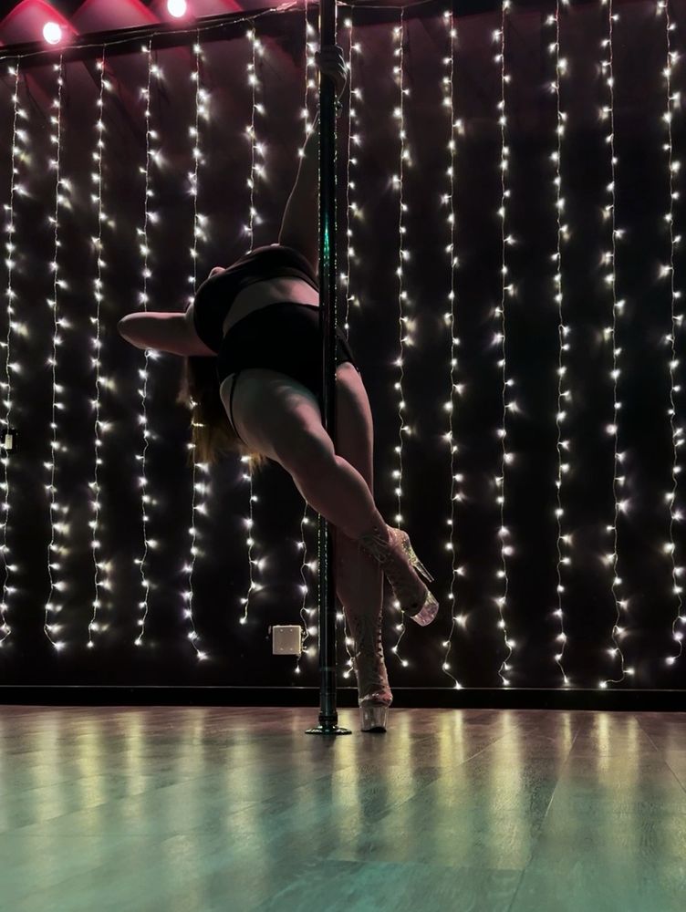 A woman leaning back while pole dancing against a backdrop of Christmas lights