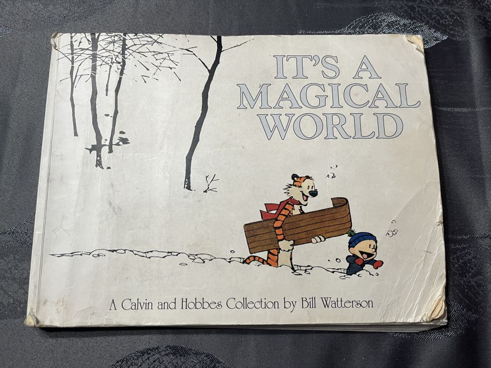The "It's a Magical World" Calvin and Hobbes collection book cover. There's some rips and bends on the cover, but it's still together and in relatively good condition.
