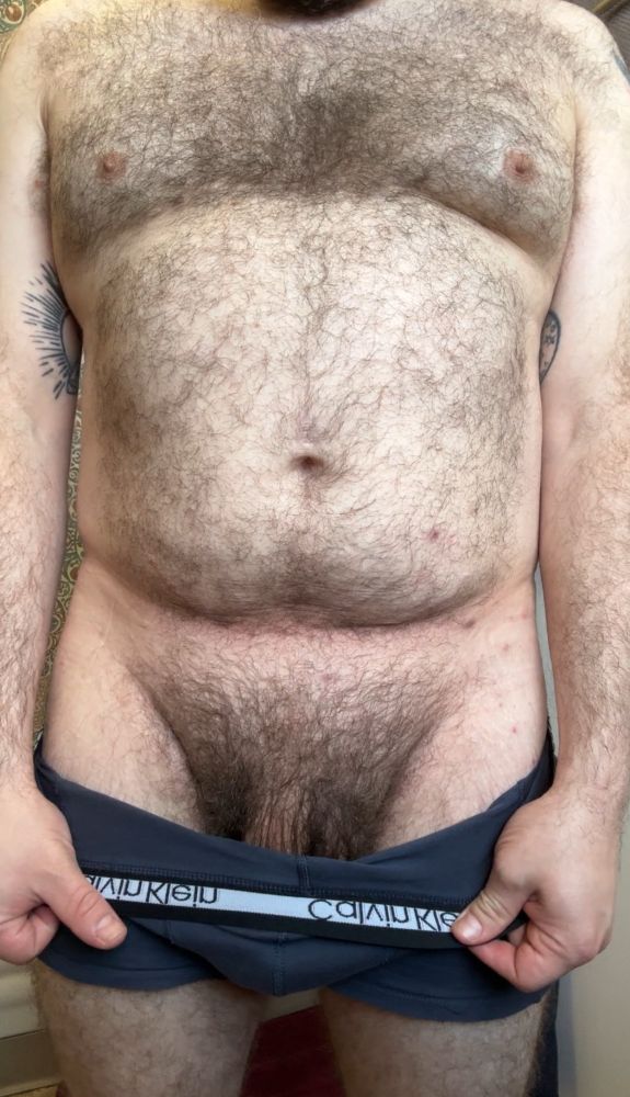 Hairy tattooed me standing nearly nude except boxer briefs. I’m pulling them down to reveal my big bush and the base of my thick soft cock. 