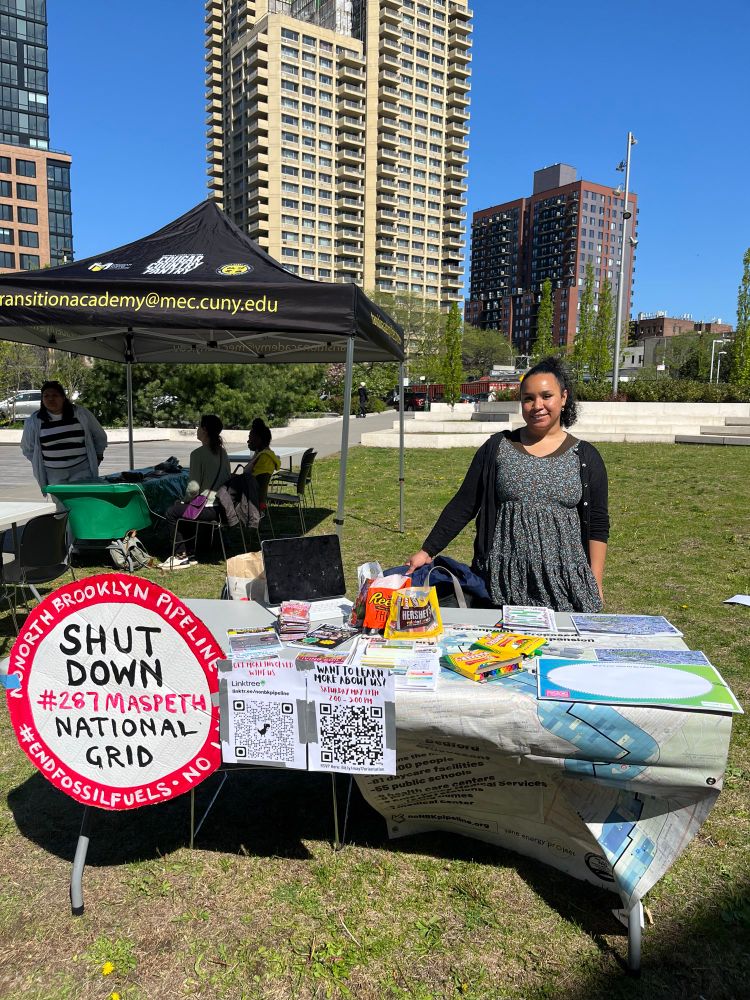 A girl at a table filled with flyers and candy with a sign that says shut down national grid 