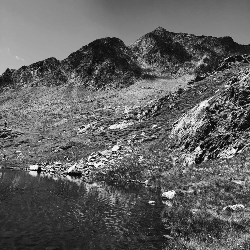 La riva di un lago alpino, un grande prato e la cima della montagna in lontananza