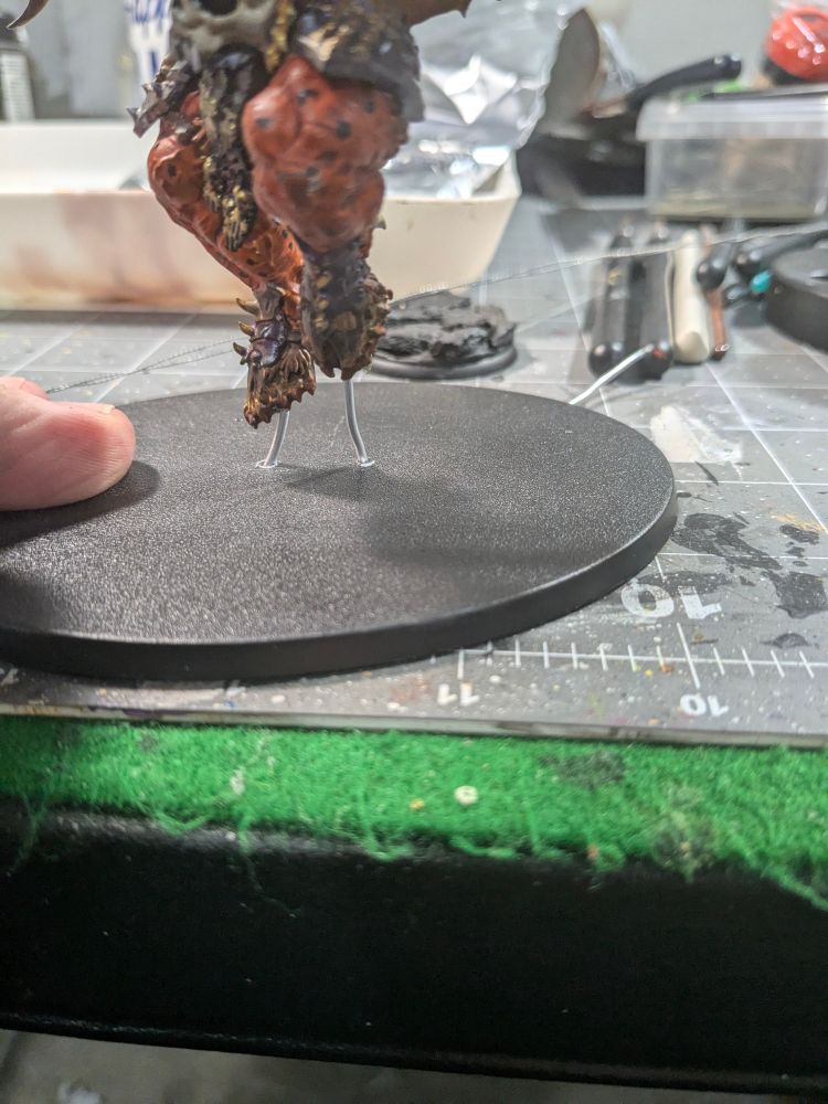 Base of bloodthirster with wires running through the base into the model.