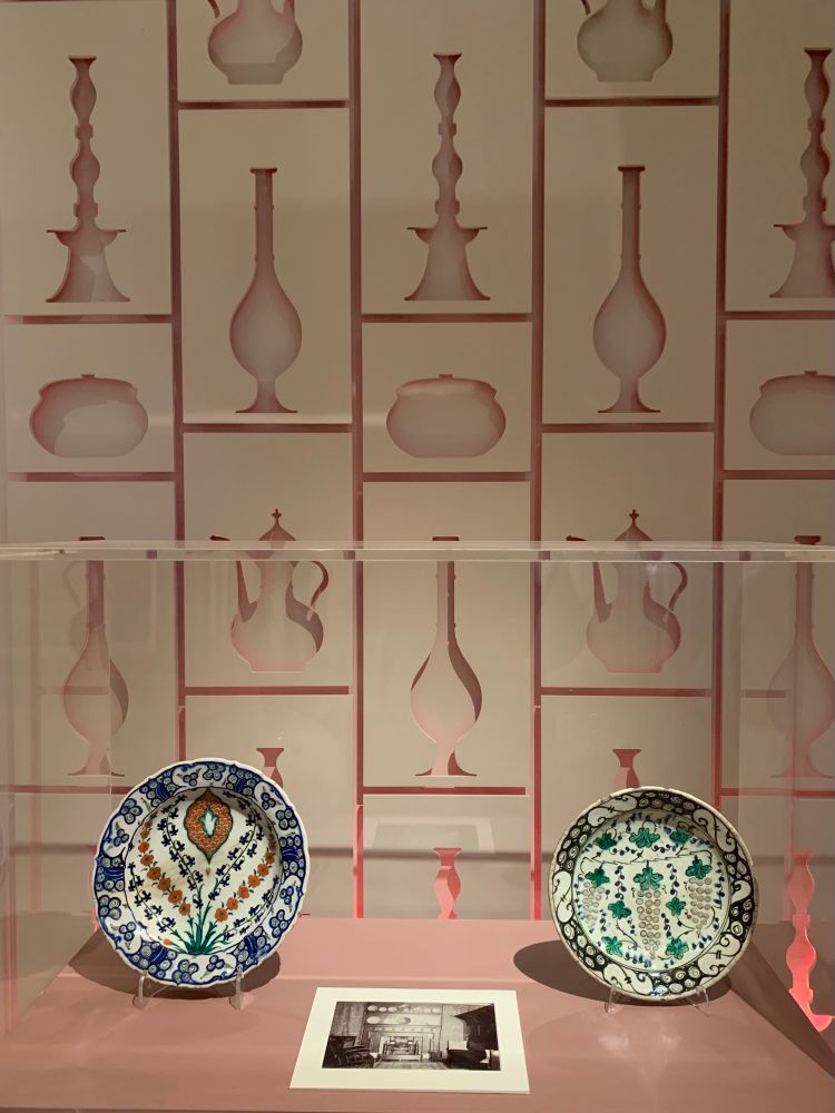 A display of two decorated plates in front of a wall with cut-out shapes of objects 