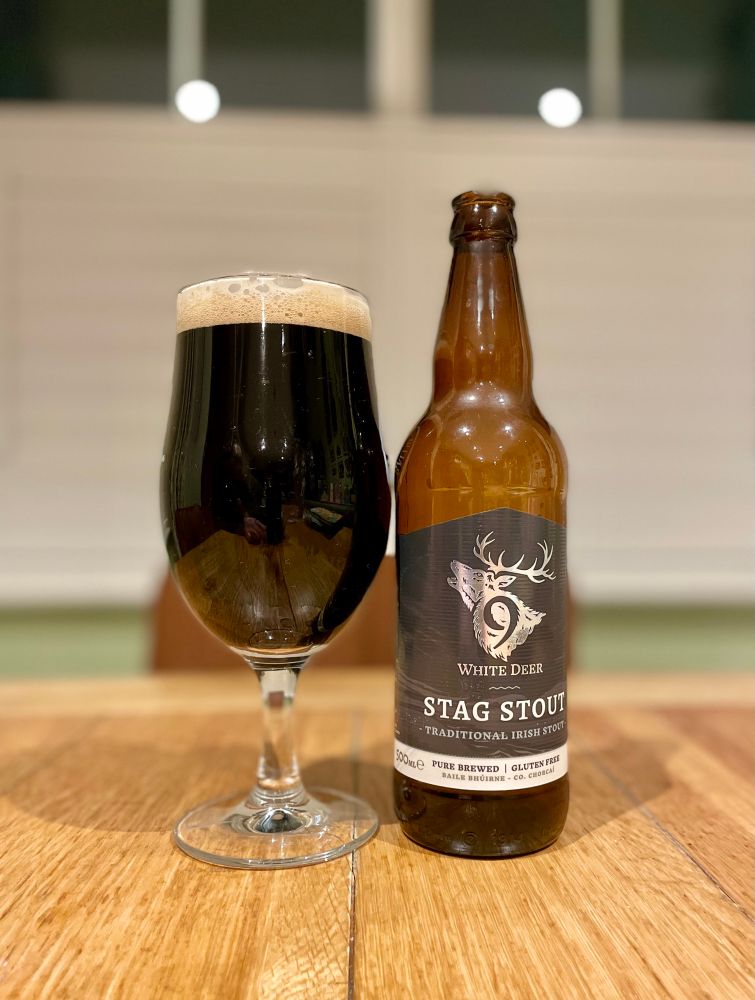 A pint glass containing 9 White Deer stag stout, and the bottle it came from standing proudly next to it. 