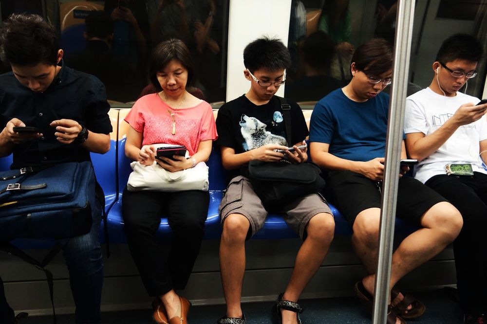 U-Bahn in Singapur. Fünf Menschen sitzen nebeneinander. Jeder guckt auf sein Handy.