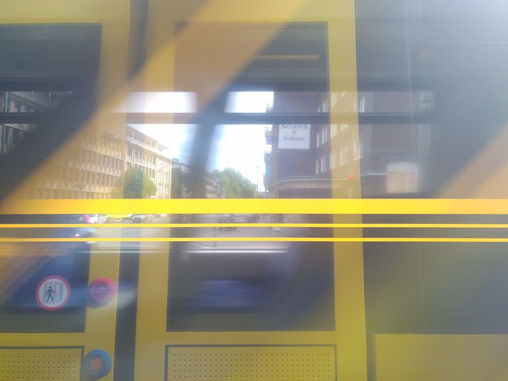 Triptychon aus drei Fotos, die aus der Straßenbahn heraus geschossen wurden beim Überqueren der Kronprinzenstraße in Essen. Bild 2 ist aufgenommen, während eine andere Straßenbahn an der des Fotografen vorbeifährt. Spiegelungen der Fensterscheiben verschwimmen dabei zu einem gelben Mosaik. 