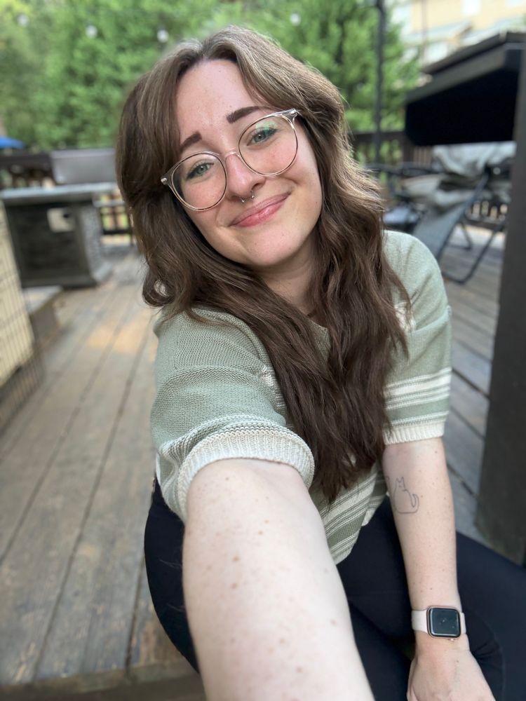 soph is sitting on her back porch with some trees in the background soft smiling in a green and white striped top. she has a fresh new haircut with some curtain bangs and is hoping it’s giving an alt punk vibe but is worried it is giving small child at recess hair vibes 