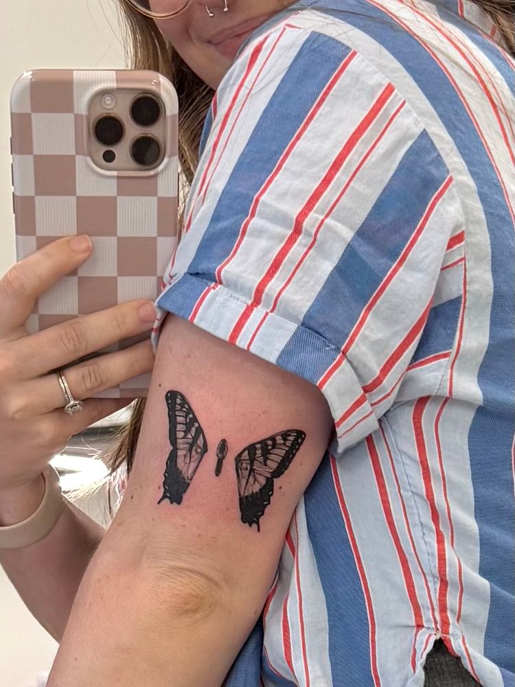 soph is posing in a mirror showing the back of her arm above her elbow. there is a brand new tattoo of a butterfly with her wings clipped from Paramore’s album Brand New Eyes