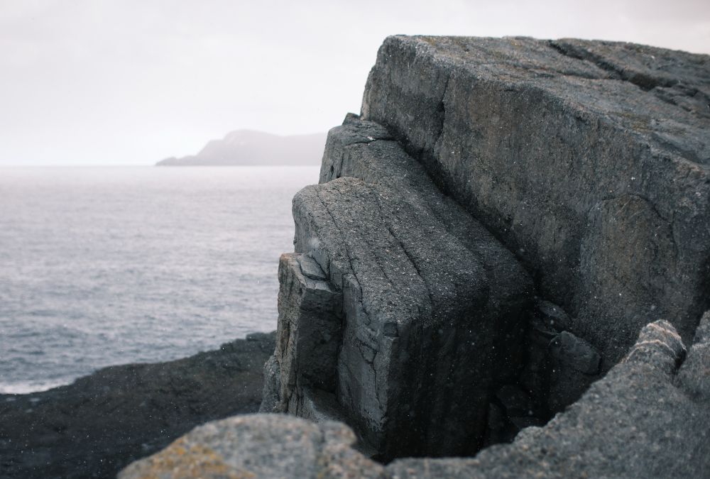 A rocky coastal Newfoundland landscape, with dramatic sweeping rocks and a hilly headland in the distance.