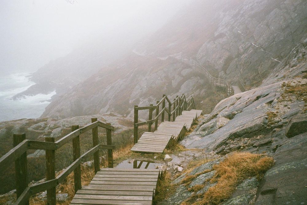 A 35mm film photo of a wooden walkway skirting the edge of a rugged coastline.
