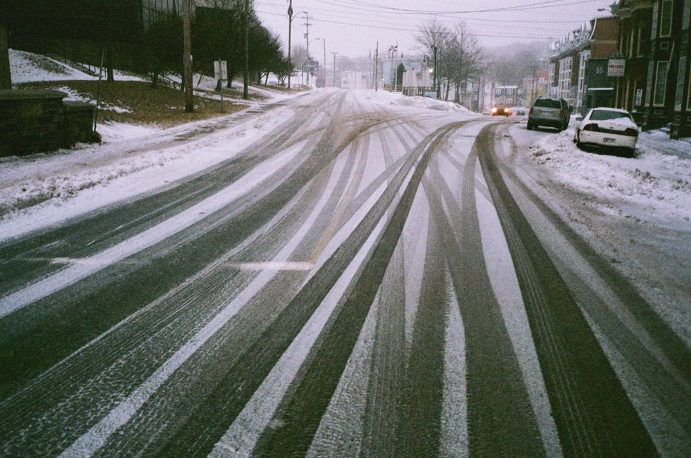 A retro-looking film photo of a snowy street in downtown St. John’s, car tracks curving into the distance.