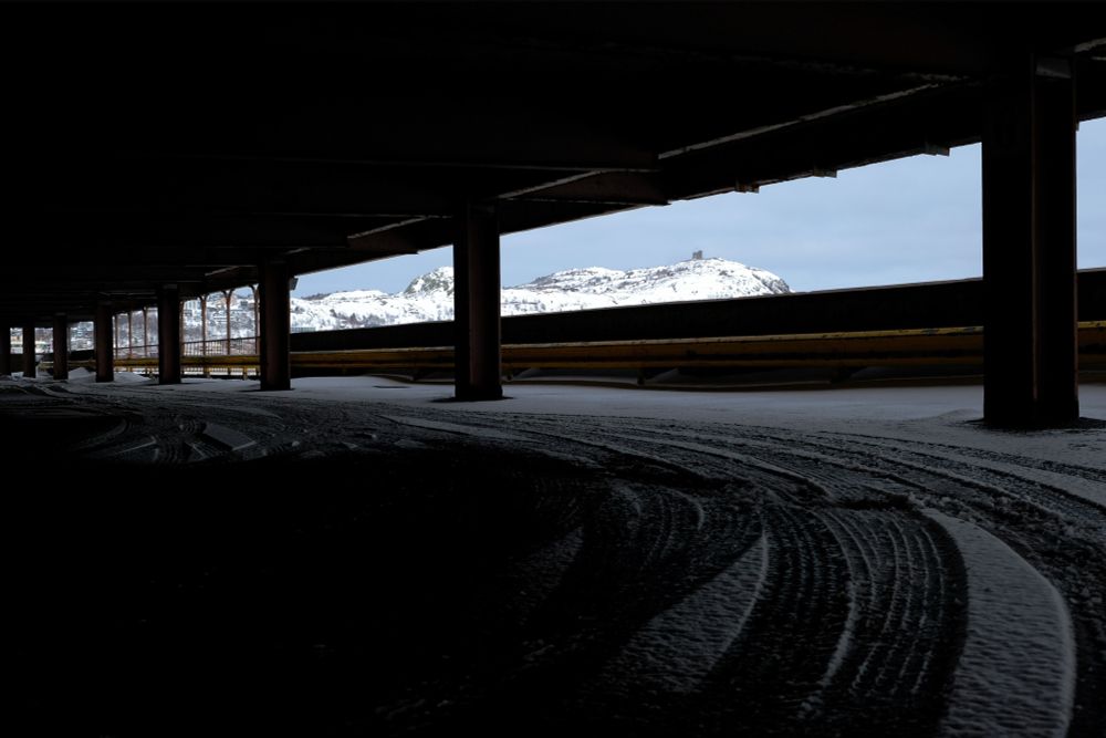 A snow-covered Signal Hill, in St. John’s, NL, seen through the open side of a parking garage, with the long slanting window creating a dramatic view of the hill.