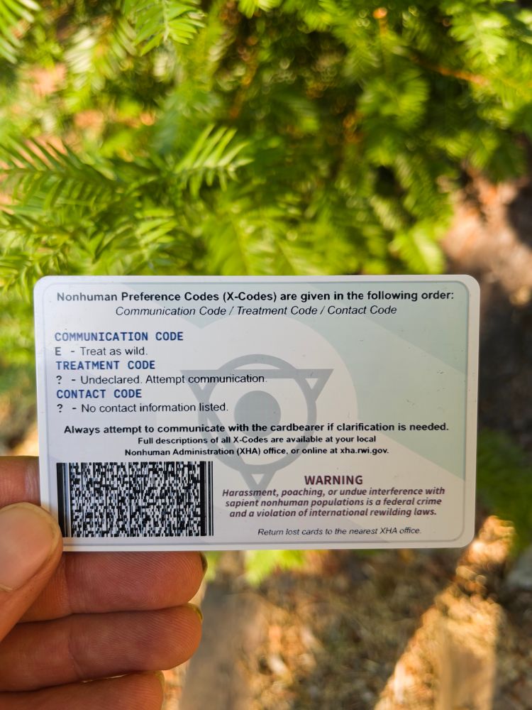 Rear of card with PDF447 2D barcode and holotherian flag watermark.

Nonhuman Preference Codes (X-Codes) are given in the following order:
Communication Code/Treatment Code/Contact Code

Communication code: E - treat as wild.
Treatment code: ? - Undeclared. Attempt communication.
Contact code: ? - No contact information listed.

Always attempt to communicate with the cardbearer if clarification is needed. Full descriptions of all X-Codes are available at your local Nonhuman Administration (XHA) field office, or online at xha.rwi.gov.

WARNING
Harassment, poaching, or undue interference with sapient nonhuman populations is a federal crime and a violation of international rewilding laws.

Return lost cards to the nearest XHA office.