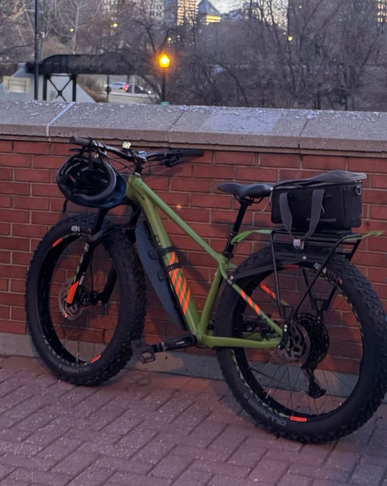 Green fat-tire bike with reflective strips leaned up against a brick wall on dry unistone
